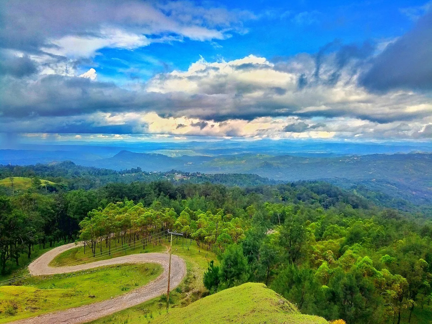 A winding road crosses green highlands beneath a dramatic sky at Fatumnasi, West Timor.