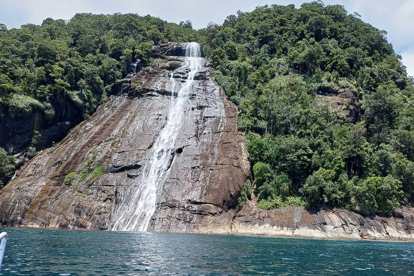 Mursala waterfall flowing over a forested granite cliff directly into the sea in North Sumatra.