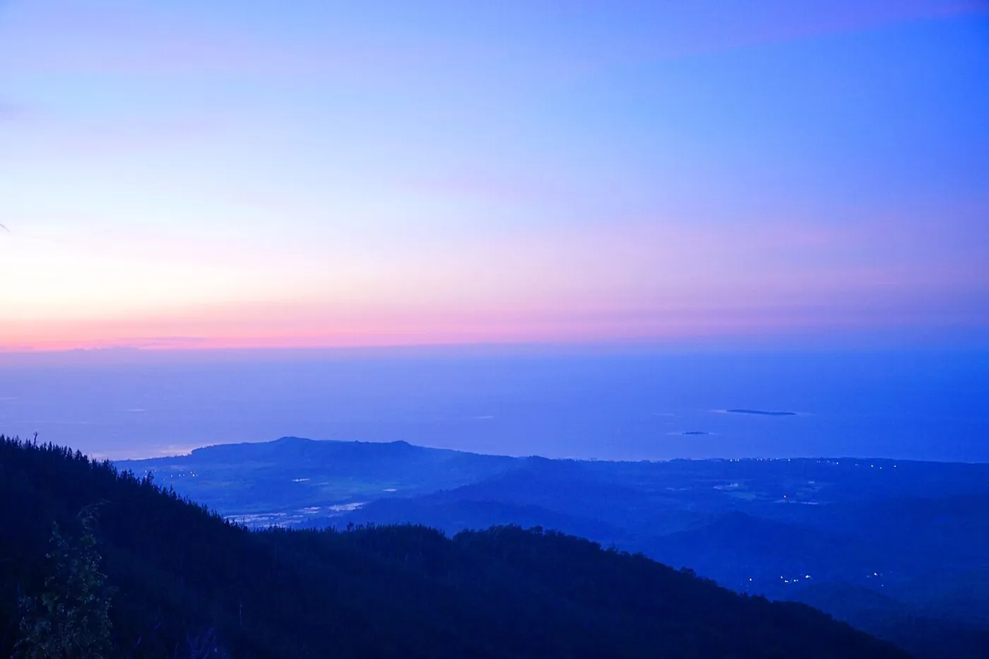 A blue and pink dusk above forested ridges, coastline and sea, photographed from Batu Gantung on Mount Tompotika