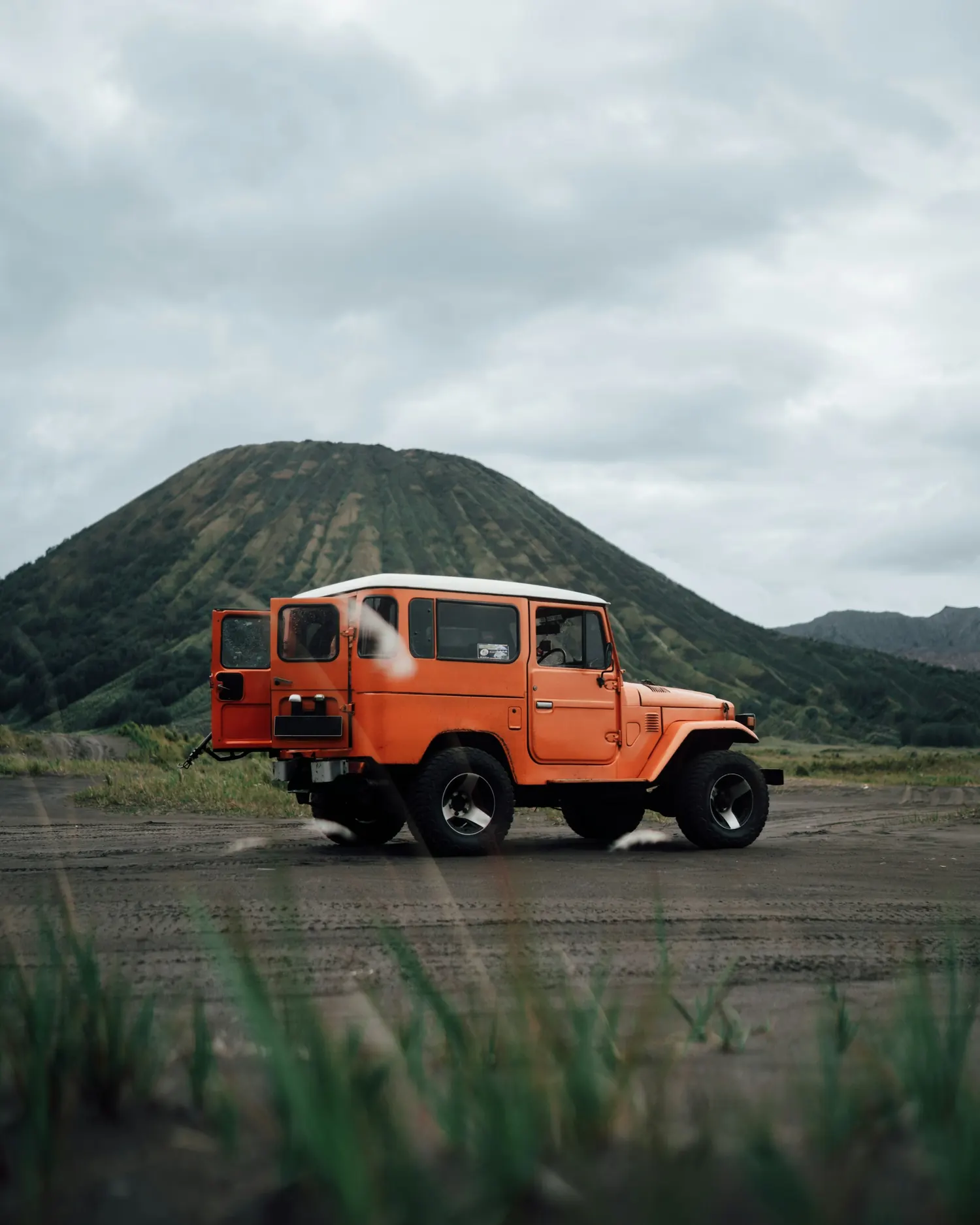 An orange jeep parked below the volcanic slopes in the Bromo landscape